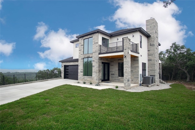 back of house featuring central AC unit, a balcony, a garage, and a yard