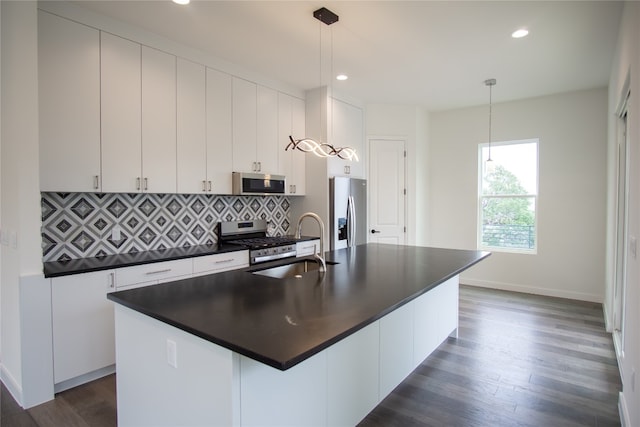 kitchen with pendant lighting, appliances with stainless steel finishes, a center island with sink, and dark hardwood / wood-style flooring