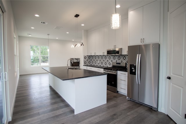 kitchen with stainless steel appliances, decorative light fixtures, an island with sink, white cabinets, and dark wood-type flooring