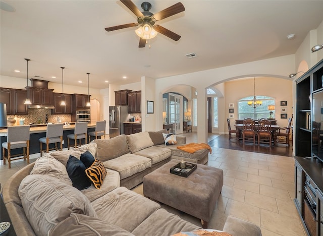 tiled living room with ceiling fan with notable chandelier