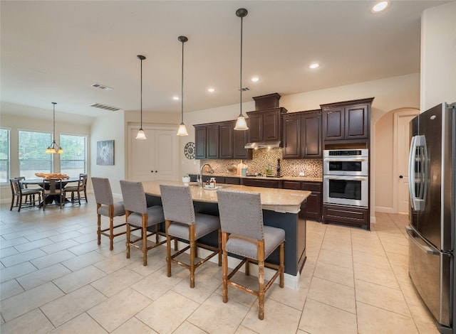 kitchen featuring light stone counters, appliances with stainless steel finishes, a kitchen breakfast bar, an island with sink, and pendant lighting