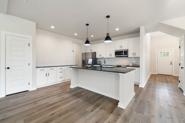 kitchen featuring sink, appliances with stainless steel finishes, decorative light fixtures, an island with sink, and dark hardwood / wood-style flooring