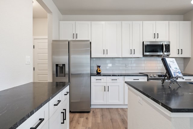 kitchen with dark stone counters, backsplash, appliances with stainless steel finishes, light hardwood / wood-style floors, and white cabinets