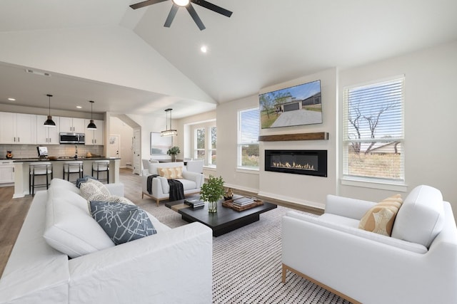 living room with light hardwood / wood-style floors, ceiling fan, and high vaulted ceiling