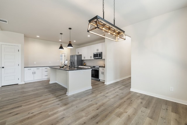 kitchen with light hardwood / wood-style flooring, a kitchen island with sink, white cabinetry, appliances with stainless steel finishes, and decorative light fixtures