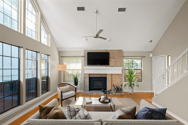 living room with light wood-type flooring, high vaulted ceiling, a brick fireplace, and ceiling fan