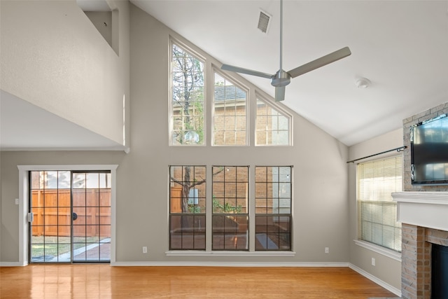 unfurnished living room with ceiling fan, plenty of natural light, light wood-type flooring, and a brick fireplace