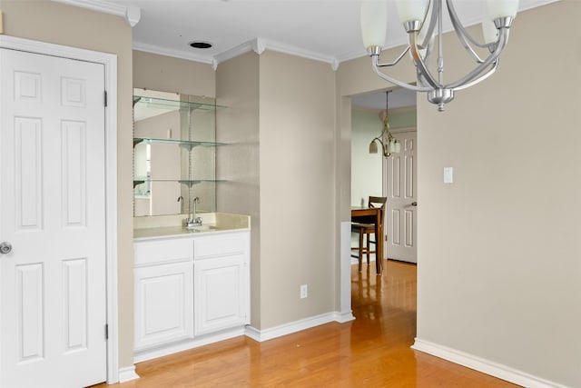 bar with white cabinetry, sink, a notable chandelier, light hardwood / wood-style floors, and ornamental molding