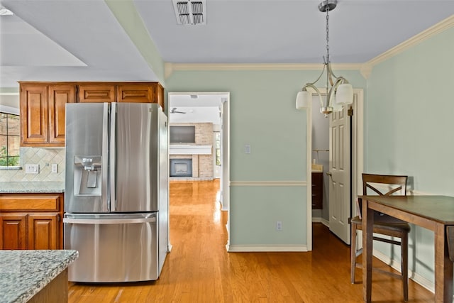 kitchen with light wood-type flooring, ornamental molding, a large fireplace, stainless steel fridge with ice dispenser, and hanging light fixtures