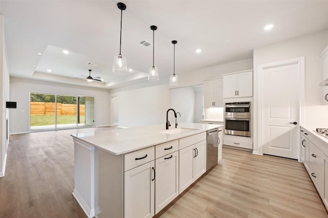 kitchen featuring a center island with sink, white cabinets, sink, ceiling fan, and a tray ceiling