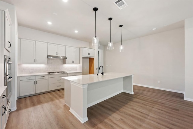 kitchen with a kitchen island with sink, decorative light fixtures, light hardwood / wood-style floors, white cabinetry, and stainless steel appliances