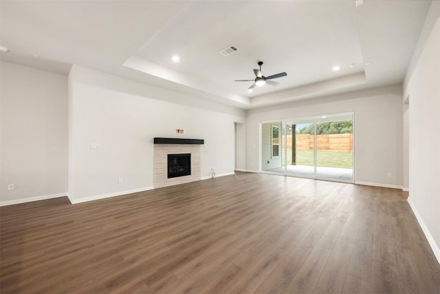 unfurnished living room with ceiling fan, dark hardwood / wood-style flooring, a tile fireplace, and a tray ceiling