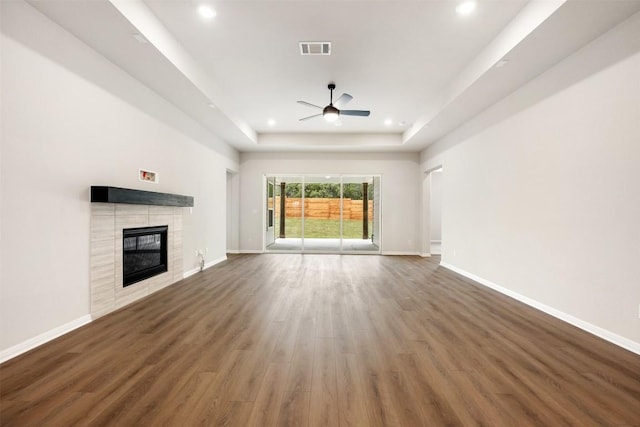 unfurnished living room featuring ceiling fan, dark hardwood / wood-style flooring, a raised ceiling, and a fireplace