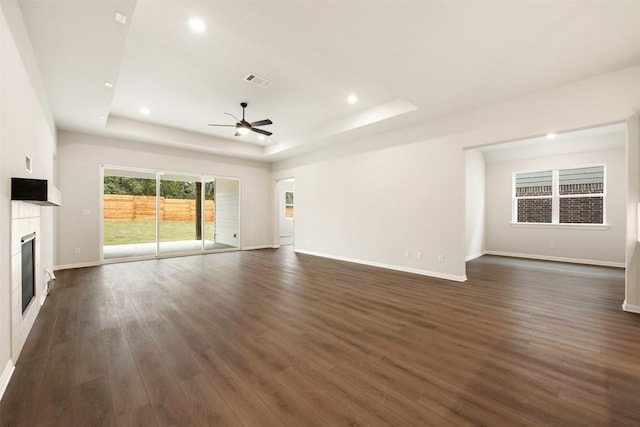 unfurnished living room with a tray ceiling, ceiling fan, and dark wood-type flooring