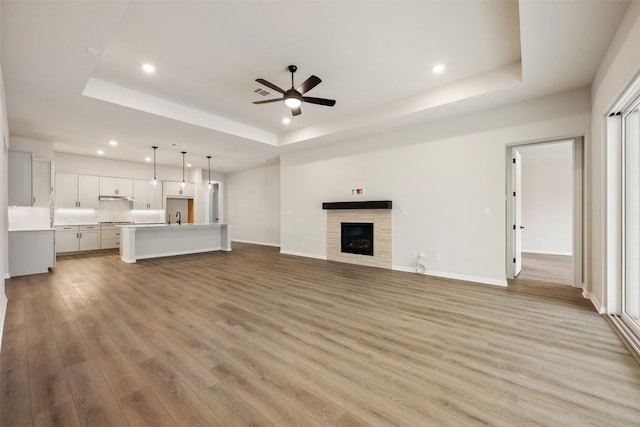 unfurnished living room with ceiling fan, light hardwood / wood-style floors, sink, and a tray ceiling