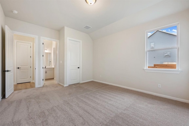 unfurnished bedroom featuring multiple windows, ensuite bathroom, light colored carpet, and vaulted ceiling