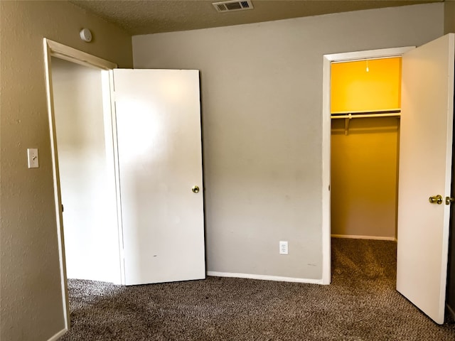 unfurnished bedroom with a closet, a spacious closet, dark carpet, and a textured ceiling