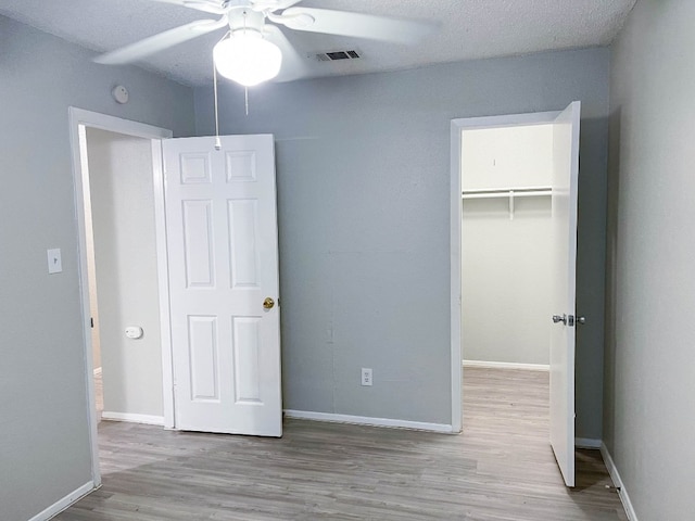 unfurnished bedroom with a closet, a spacious closet, light wood-type flooring, a textured ceiling, and ceiling fan