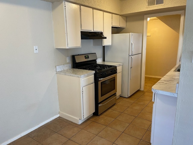 kitchen featuring white cabinets, white refrigerator, stainless steel range with gas cooktop, and light tile patterned floors