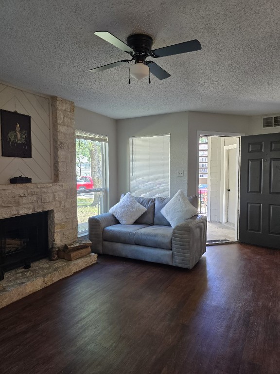 living room featuring a fireplace, a textured ceiling, dark hardwood / wood-style flooring, and ceiling fan