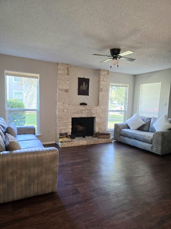 living room featuring a textured ceiling, ceiling fan, a stone fireplace, and dark wood-type flooring