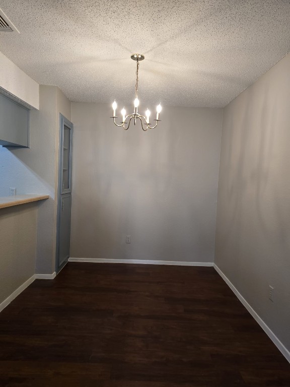 unfurnished dining area with dark wood-type flooring, a textured ceiling, and a notable chandelier