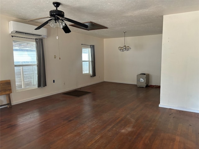 spare room with dark wood-type flooring, a textured ceiling, a wall mounted air conditioner, and ceiling fan with notable chandelier