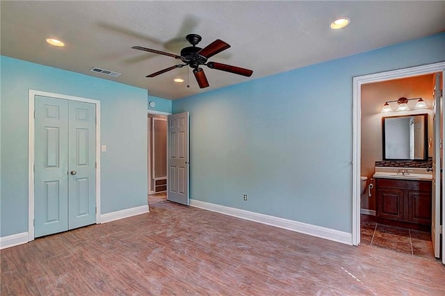 unfurnished bedroom featuring light wood-type flooring, ensuite bathroom, ceiling fan, sink, and a closet