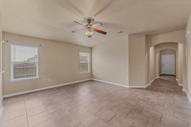 empty room featuring a textured ceiling, light tile patterned floors, and ceiling fan