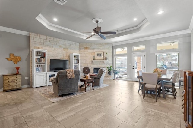 living room featuring ornamental molding, a tray ceiling, and a stone fireplace