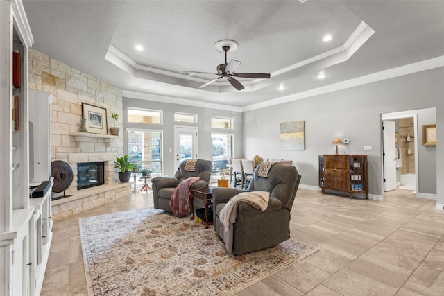 living room with ceiling fan, ornamental molding, a stone fireplace, and a raised ceiling