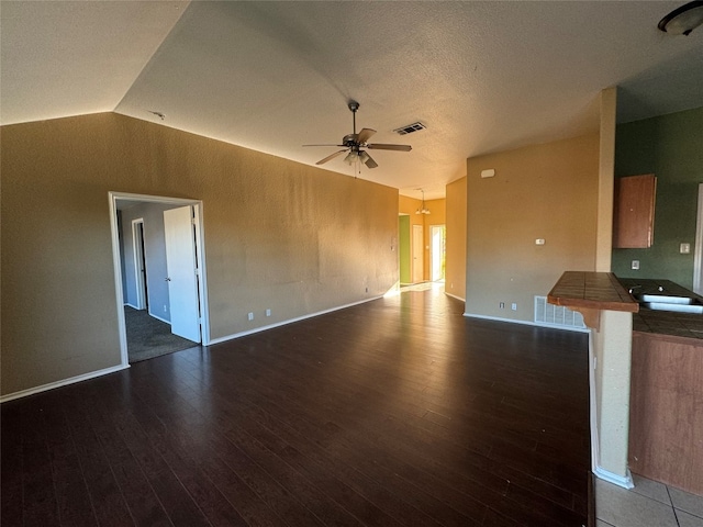 unfurnished living room featuring dark wood-type flooring, vaulted ceiling, ceiling fan, and a textured ceiling