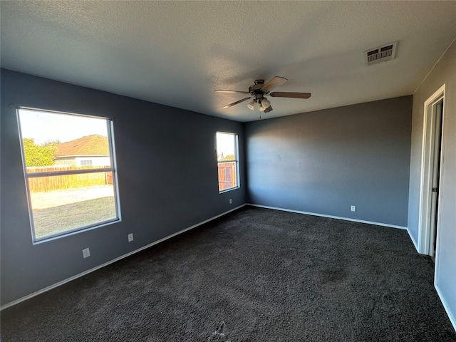 unfurnished room with a textured ceiling, a healthy amount of sunlight, and dark carpet