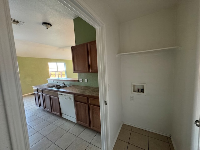 kitchen featuring sink, white dishwasher, light tile patterned floors, tile counters, and vaulted ceiling