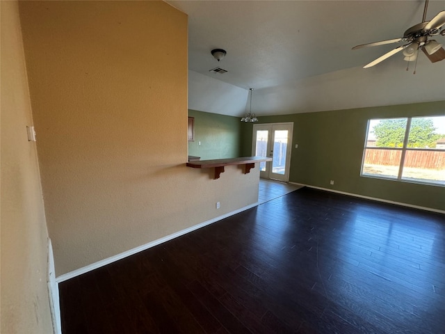 spare room featuring ceiling fan with notable chandelier, dark wood-type flooring, and vaulted ceiling