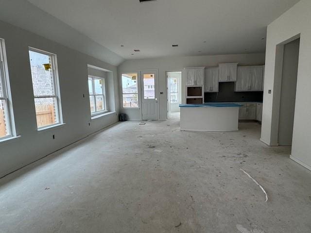 interior space featuring a kitchen island, lofted ceiling, white cabinets, stainless steel microwave, and open floor plan