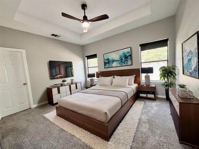 carpeted bedroom with ceiling fan, a raised ceiling, and multiple windows