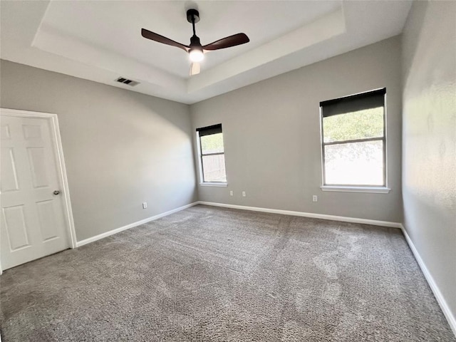 carpeted spare room with a raised ceiling and ceiling fan