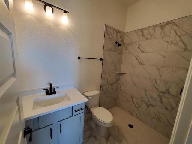 bathroom featuring a tile shower, vanity, and toilet