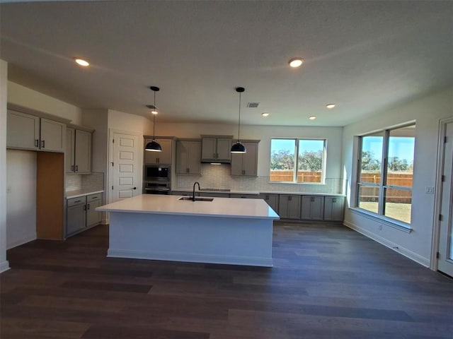 kitchen with gray cabinetry, stainless steel appliances, a kitchen island with sink, sink, and pendant lighting