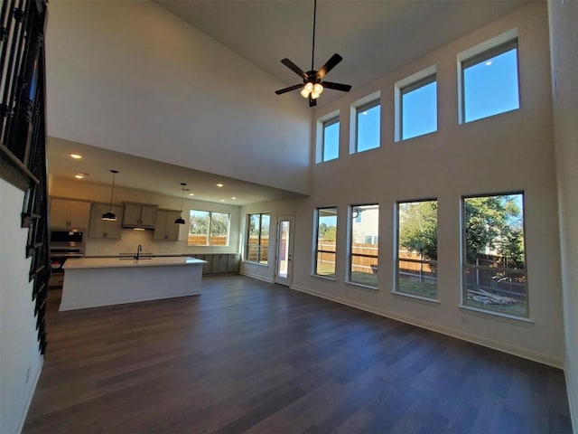 unfurnished living room with a towering ceiling, dark hardwood / wood-style flooring, ceiling fan, and sink