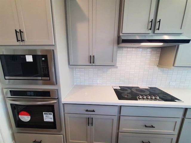 kitchen featuring gray cabinets, stainless steel appliances, range hood, and tasteful backsplash