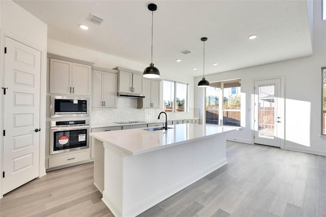 kitchen featuring sink, light wood-type flooring, appliances with stainless steel finishes, pendant lighting, and a kitchen island with sink