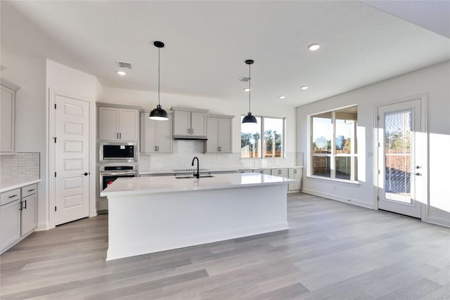 kitchen with sink, hanging light fixtures, appliances with stainless steel finishes, a healthy amount of sunlight, and a kitchen island with sink