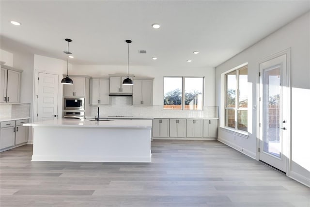 kitchen featuring gray cabinets, stainless steel appliances, tasteful backsplash, an island with sink, and decorative light fixtures