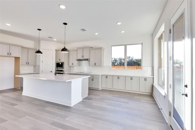 kitchen with pendant lighting, a center island, black electric stovetop, light hardwood / wood-style floors, and decorative backsplash