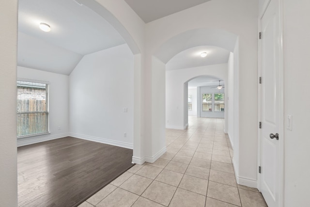 corridor with light hardwood / wood-style floors, a healthy amount of sunlight, and vaulted ceiling