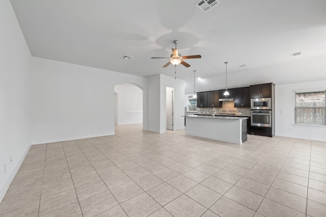 kitchen with stainless steel appliances, a center island with sink, light tile patterned floors, tasteful backsplash, and ceiling fan