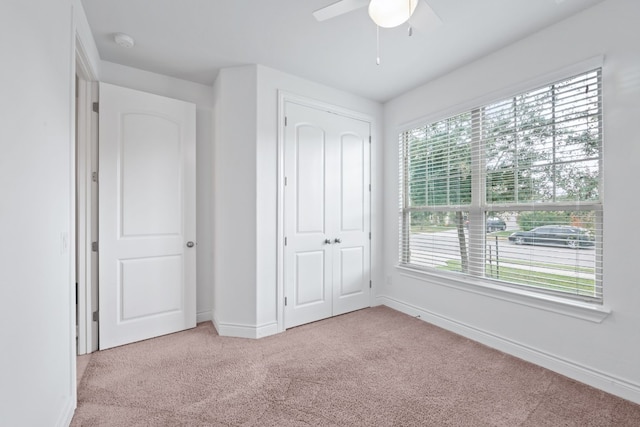 unfurnished bedroom with light colored carpet, multiple windows, ceiling fan, and a closet