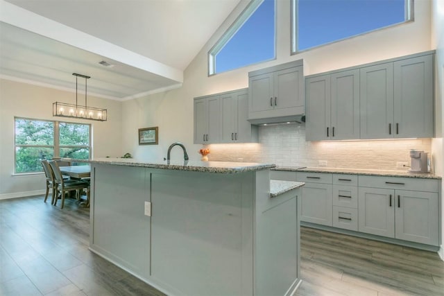 kitchen with light stone countertops, pendant lighting, gray cabinets, decorative backsplash, and a center island with sink